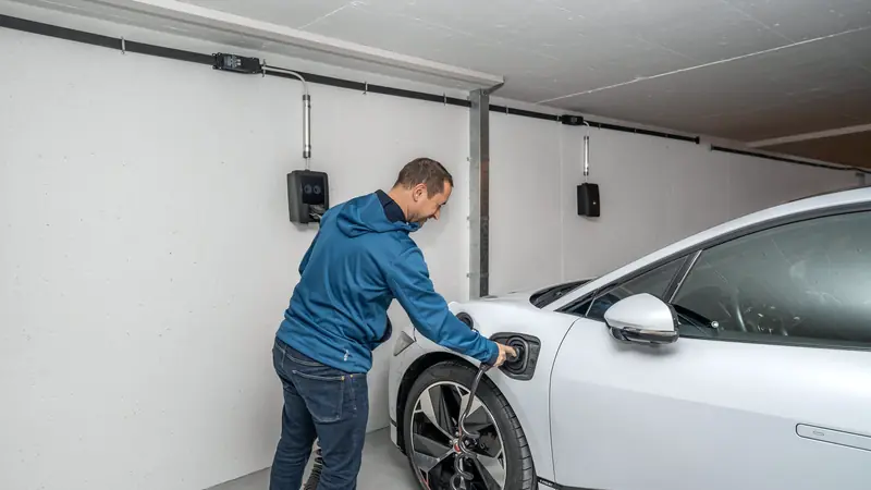 Homme qui branche sa voiture électrique sur une borne murale dans son garage