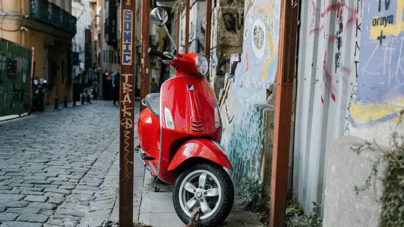 Scooter rouge garé dans une ruelle pavée