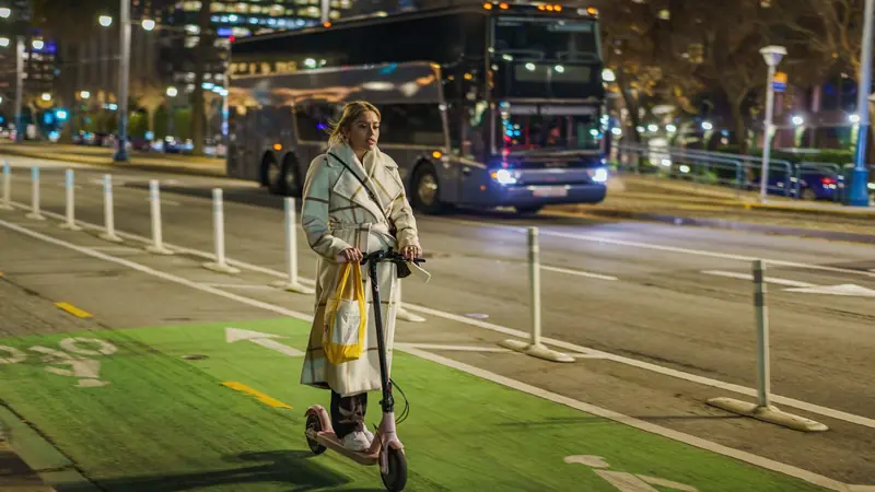 Personne qui roule en trottinette électrique sur une piste cyclable le soir
